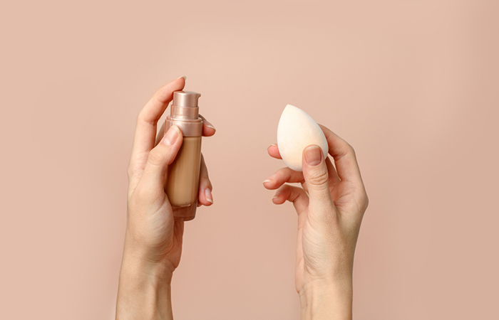 Close up of a woman's hands holding a concealer and a makeup sponge to cover the varicose veins