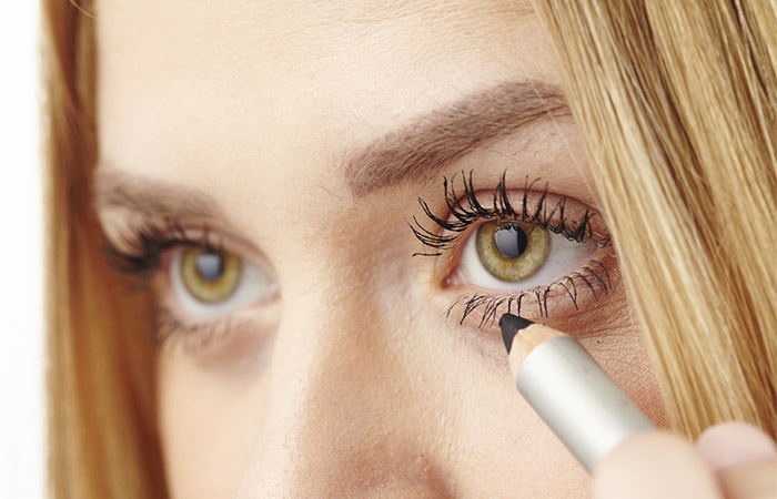 Woman applying kohl to lower lids of her eyes for a contrasting effect against the brightness of a yellow dress