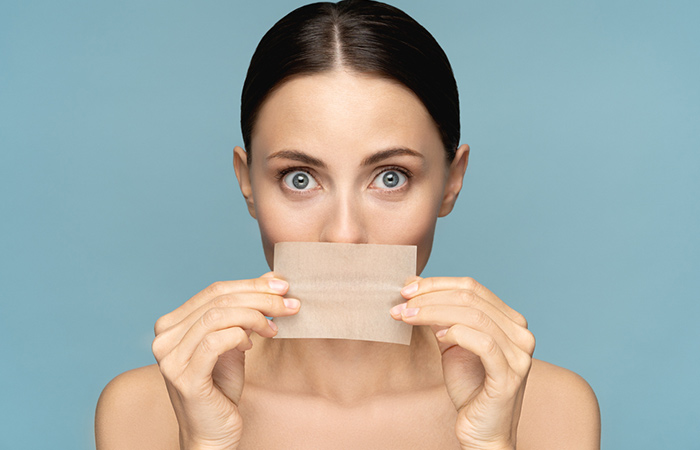 A closeup of a woman blotting her lips to prevent lipstick transferring.